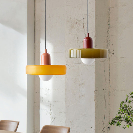 Zwei moderne Hängelampen aus Glas, gelb und grün, über einem Esstisch, minimalistisches Design.