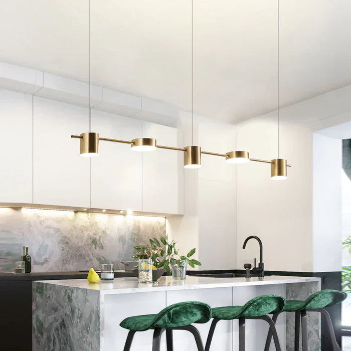 Moderne goldene Pendelleuchte über Kücheninsel mit grünen Samtstühlen und Marmorarbeitsplatte.
