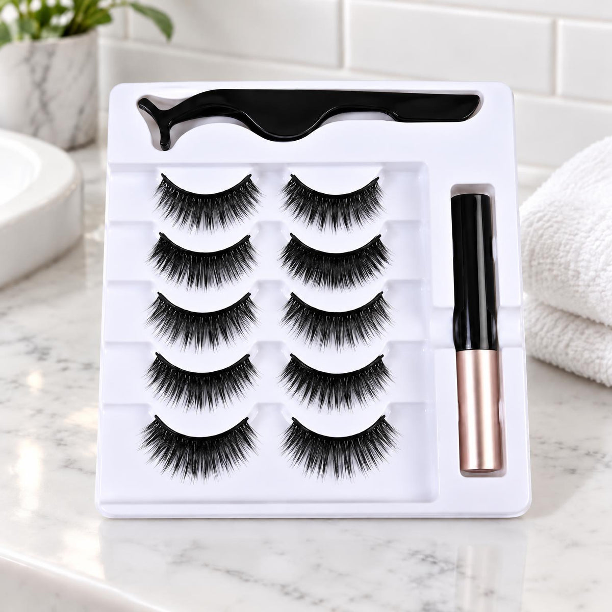 Fem par fransar i medelfyllig stil, pincett och eyeliner i vit bricka vid handdukar 11