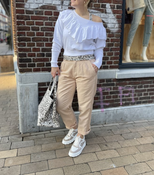 Frau in weißem Rüschenpullover, beigen Hosen, Leopardenmuster-Tasche und Sneakers auf Straße.