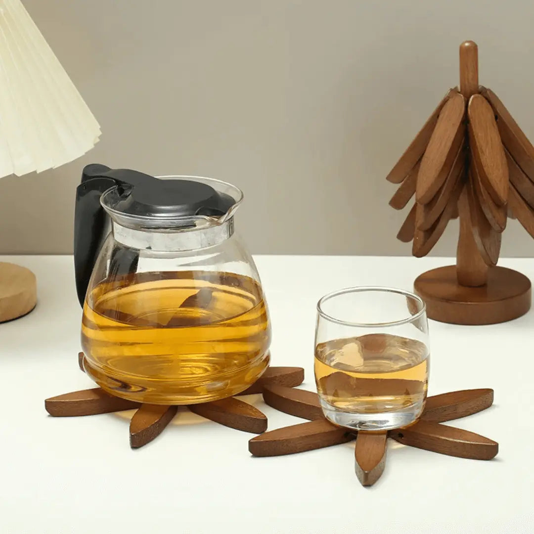 Glaskaraffe mit schwarzem Griff und Glas auf Holzuntersetzern, gefüllt mit Tee, auf weißem Tisch.