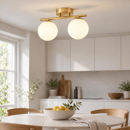 Lampa med två glaskulor på mässingsfärgad skena ovanför matbord med citronskål i ljust kök 2