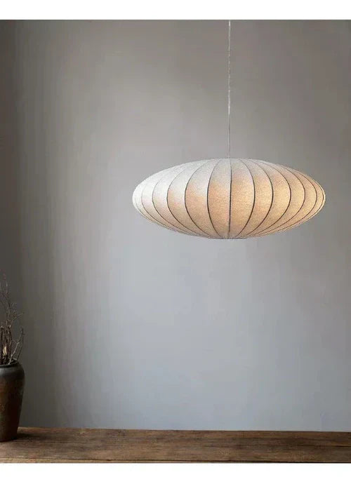 Moderne weiße Pendelleuchte aus Stoff, oval, hängend über Holztisch, minimalistisches Design.