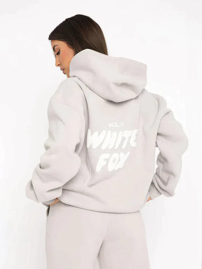 Frau in grauem Hoodie mit "White Fox" Aufdruck, Kapuze, lässiger Stil, Rückansicht.