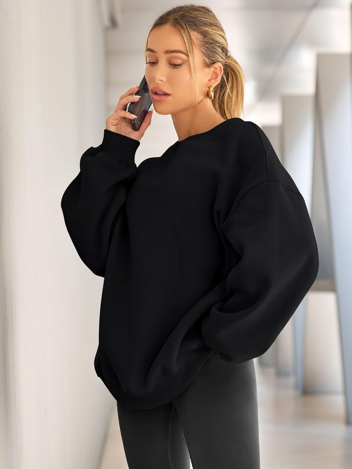 Frau in schwarzem Oversize-Pullover telefoniert, modisch, lässig, Herbstmode, Innenraum.