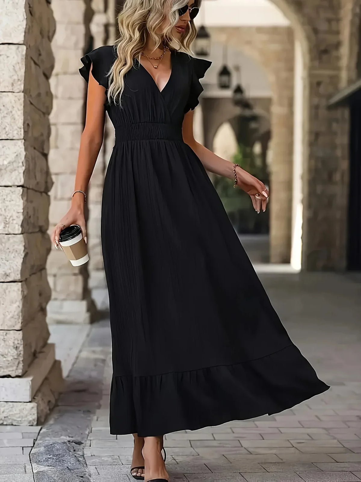 Frau in schwarzem Maxikleid mit Kaffeebecher, elegante Mode, Sommerkleid, Stadtbummel.