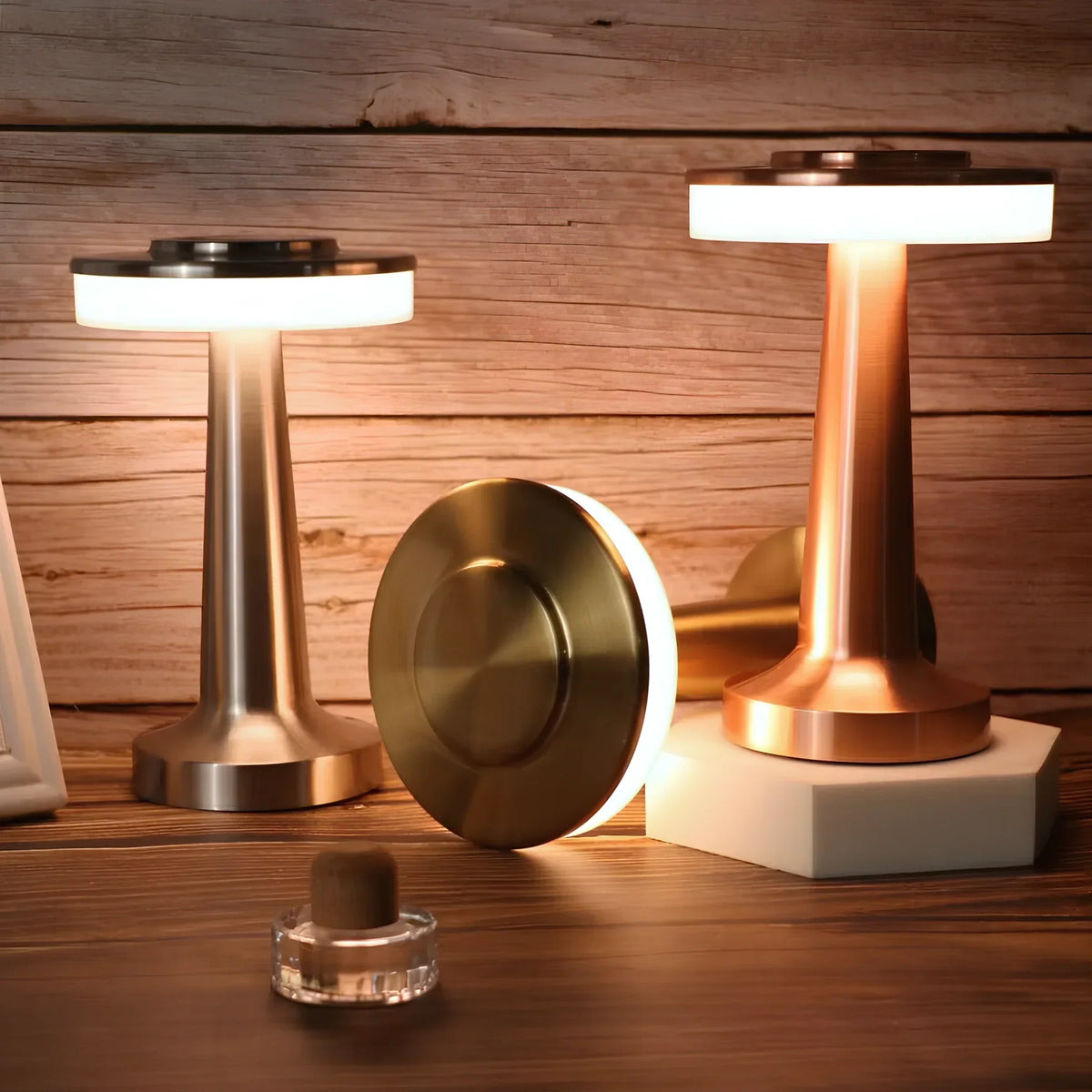 Moderne LED-Tischlampen aus Metall in Gold und Silber auf Holzoberfläche, warmweißes Licht.