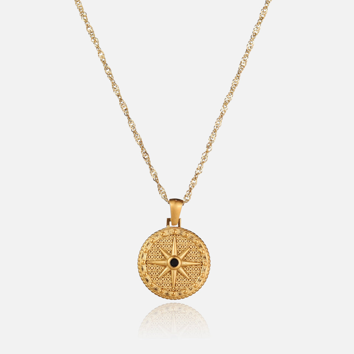 Guldfärgat halsband med rund hängsmycke format som en åttauddig stjärna med en liten svart sten i mitten, sett framifrån mot ljus bakgrund. 1