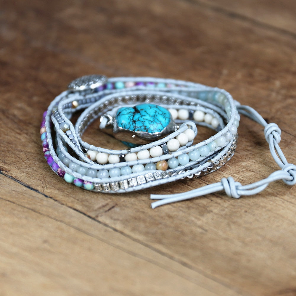 Mehrlagiges Armband mit türkisfarbenem Stein, Perlen und Lederband auf Holzoberfläche.