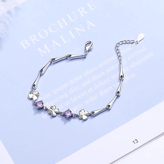 Silberarmband mit Kleeblatt- und lila Kristallanhängern, elegantes Schmuckdesign.