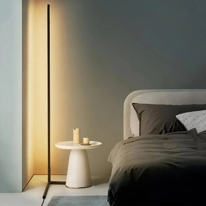 Tänd golvlampa med varmt sken bredvid ett vitt sidobord och en säng med mörkt sänglinne 1