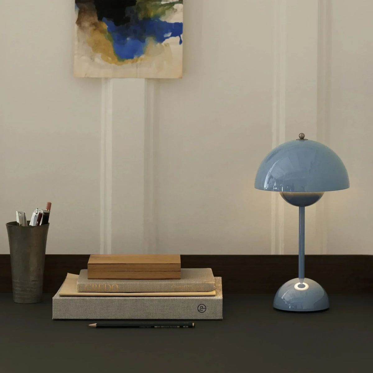 Blaue Tischlampe aus Metall auf Schreibtisch mit Büchern und Stiften, modernes Design.