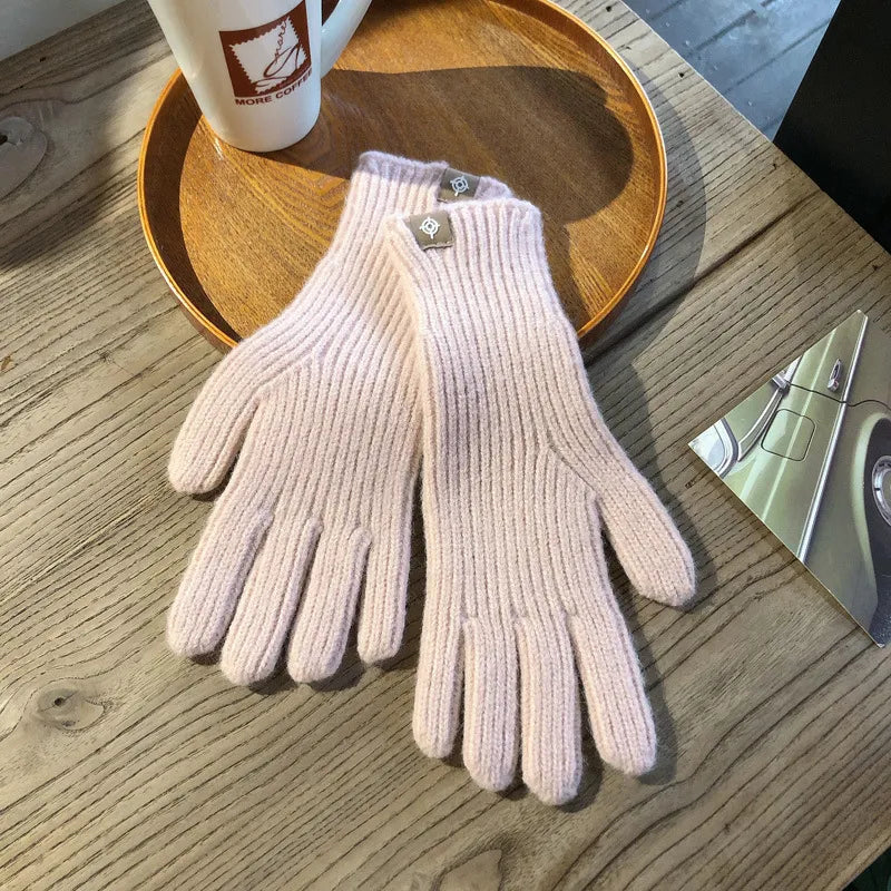 Rosa Strickhandschuhe aus Wolle auf Holztisch neben Kaffeetasse und Foto.