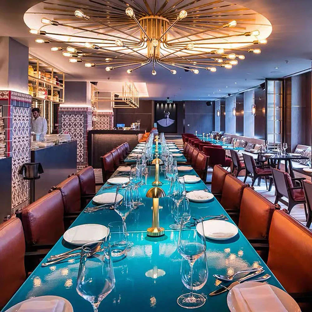 Luxuriöses Restaurant mit langem, türkisfarbenem Tisch, modernen Leuchten und eleganten Sitzgelegenheiten.