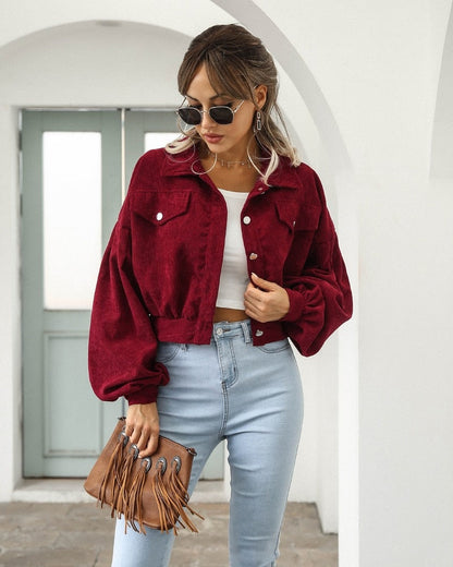 Frau in roter Cordjacke, blauer Jeans, Sonnenbrille, braune Fransenhandtasche, modisch.