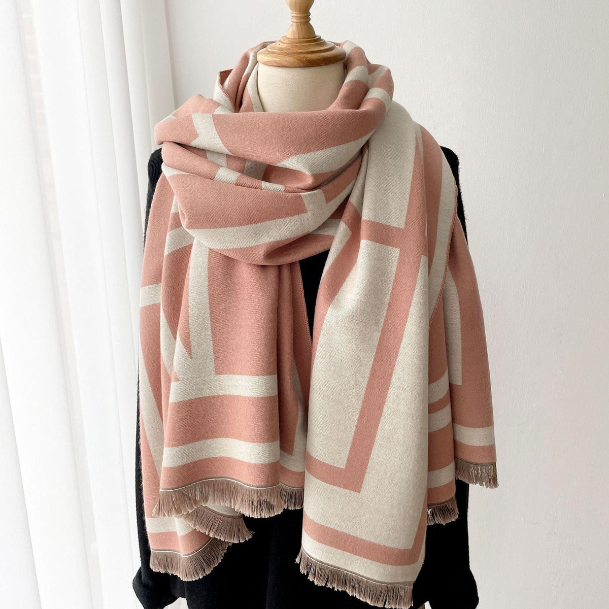 Rosa-weißer Wollschal mit geometrischem Muster auf schwarzem Mantel, modisches Accessoire.