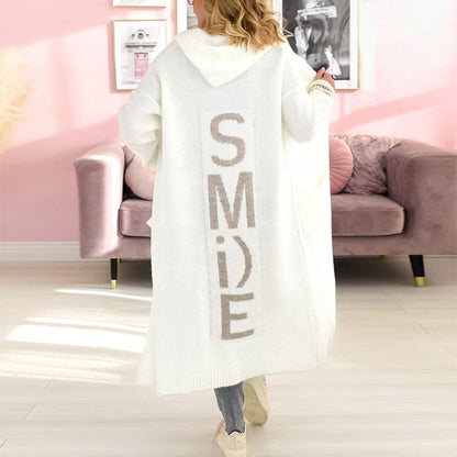 Frau in weißem Strickmantel mit "SMILE"-Aufdruck, Kapuze, lässiger Stil, Wohnzimmer.
