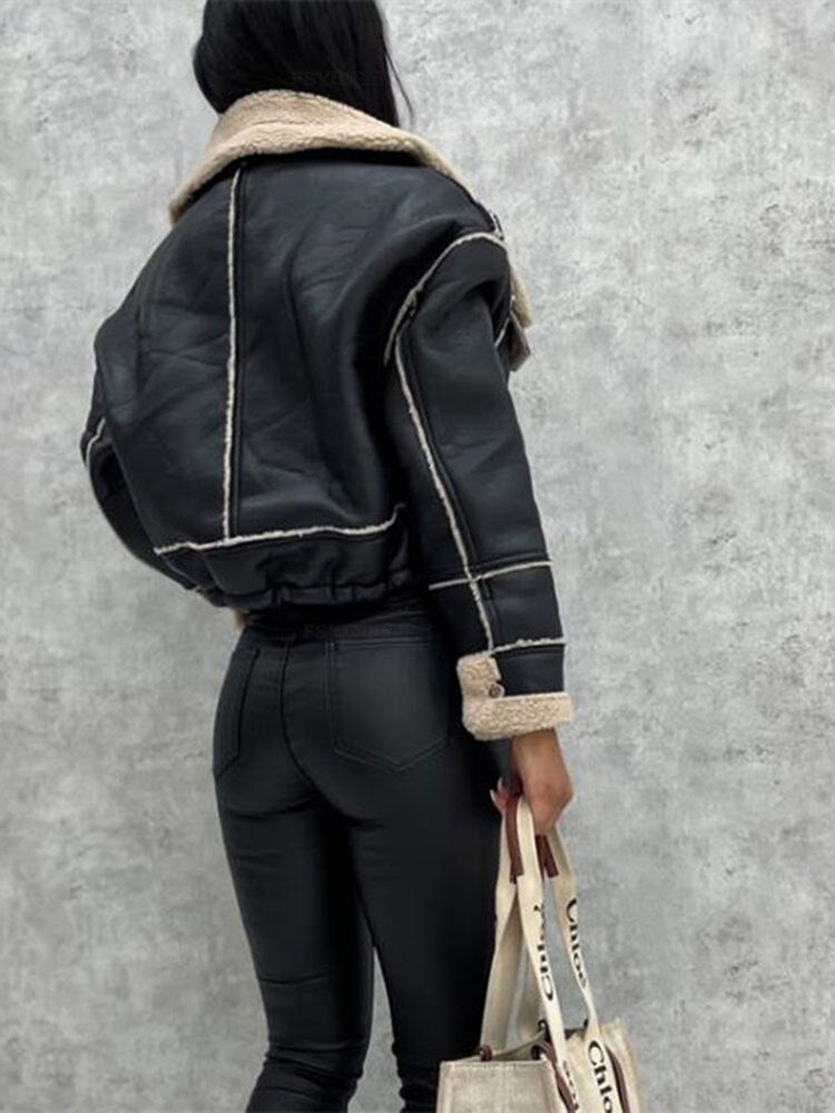 Frau in schwarzer Lederjacke mit Fellkragen, hält Stofftasche, grauer Hintergrund.