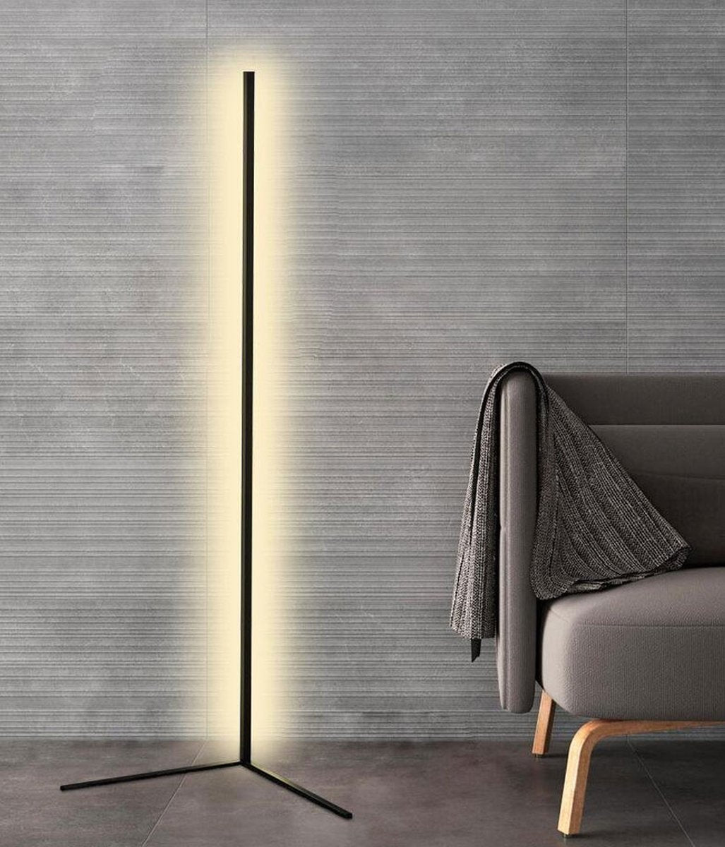 Svart golvlampa med mjukt varmvitt sken framför en grå strukturerad vägg, bredvid en fåtölj med pläd 8