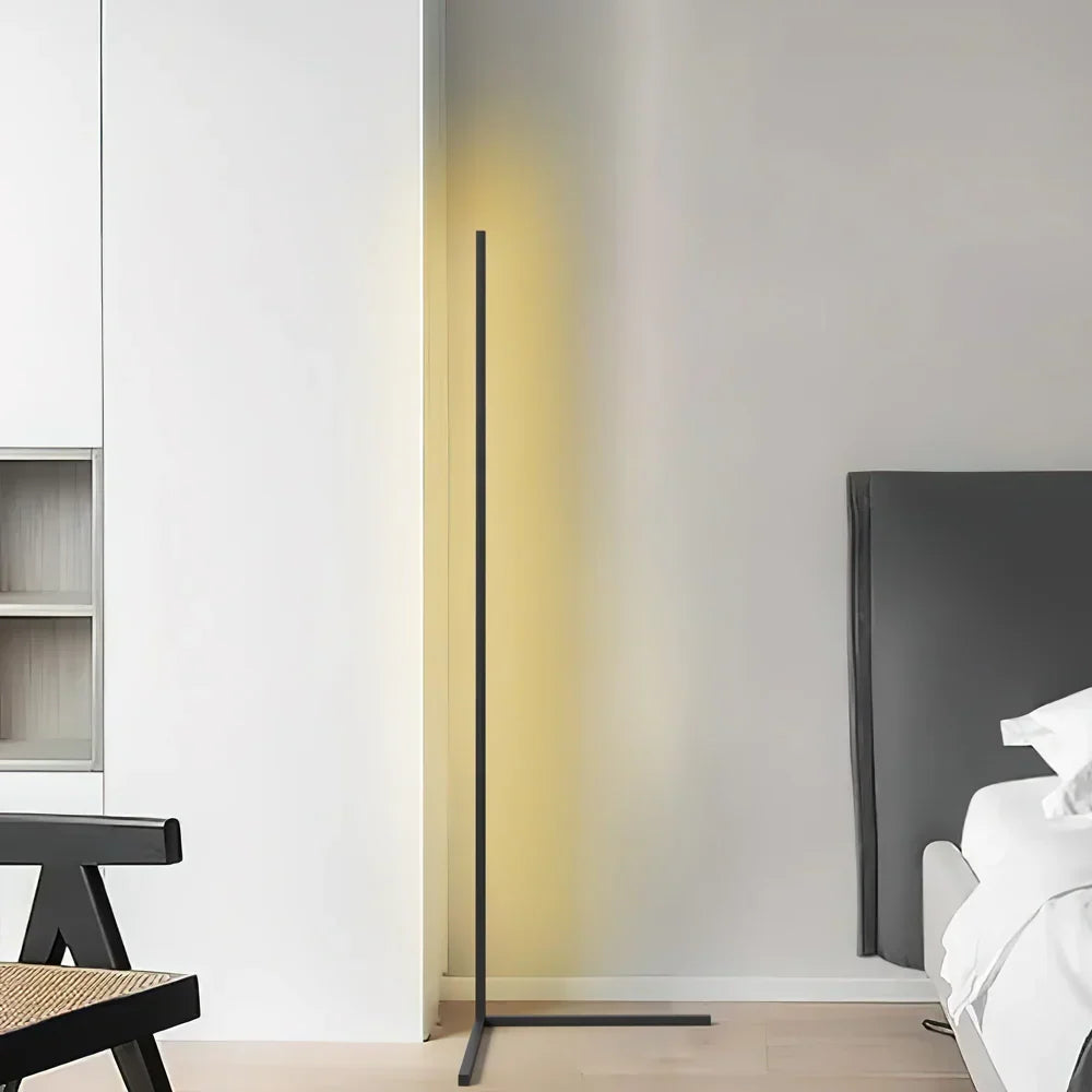 Svart golvlampa med gulaktigt sken i ett ljust rum, med en stol och en säng i kanten 7