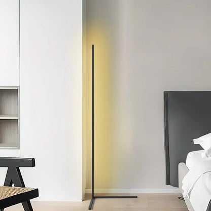 Svart golvlampa med gulaktigt sken i ett ljust rum, med en stol och en säng i kanten 7