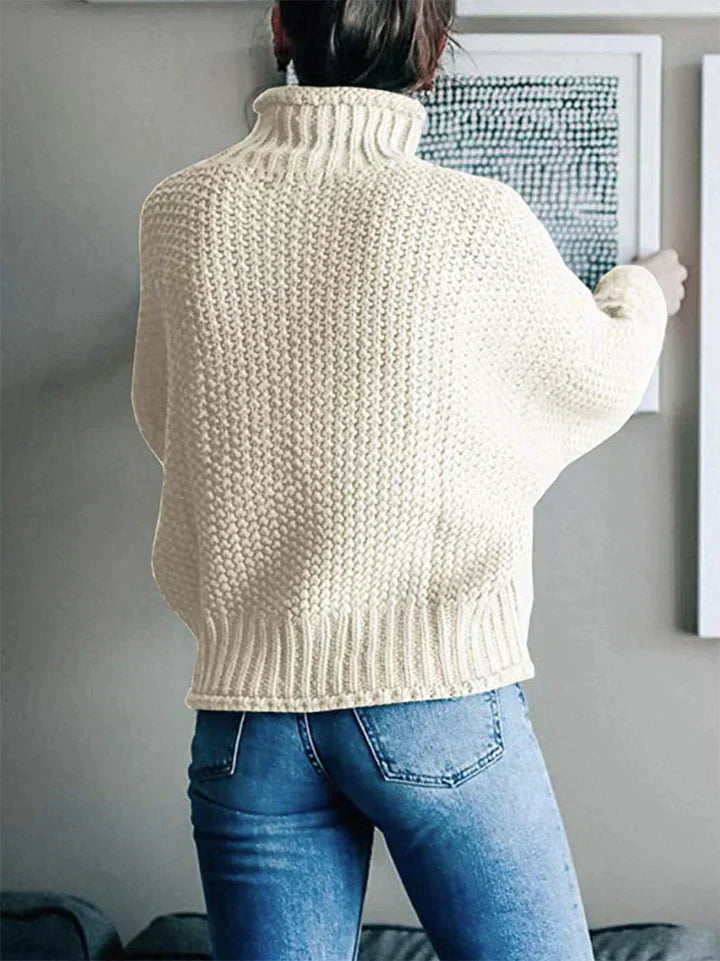 Frau in cremefarbenem Strickpullover und blauer Jeans betrachtet Wandkunst.