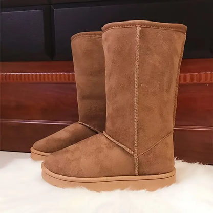 Braune Wildleder-Stiefel, kniehoch, auf weißem Teppich vor Holzwand.
