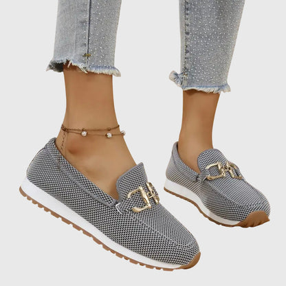 Grå mesh-loafers med guldfärgat spänne sedda från sidan, ena foten lyft på modell 3