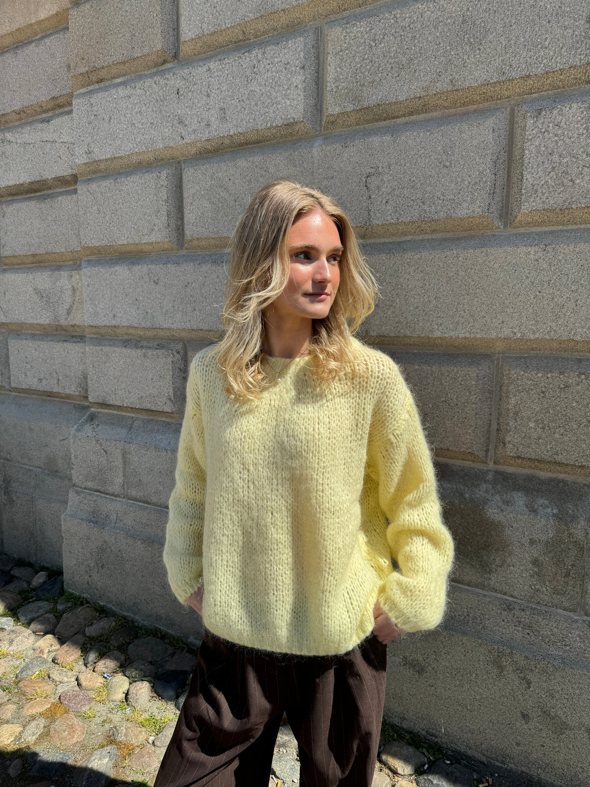 Frau in gelbem Strickpullover vor Steinwand, modisch, Herbstmode, lässiger Stil.