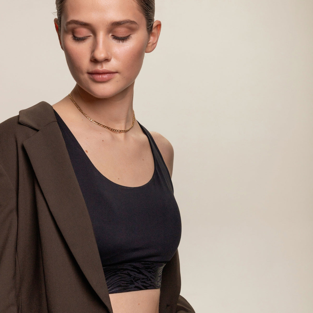 Frau mit goldener Figaro-Kette, schwarzem Top und braunem Blazer.