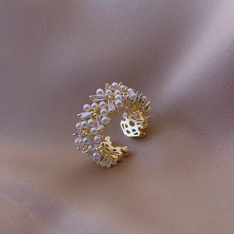 Goldener Ring mit Perlen und Kristallen auf beigem Stoff, eleganter Schmuck, luxuriöses Design.