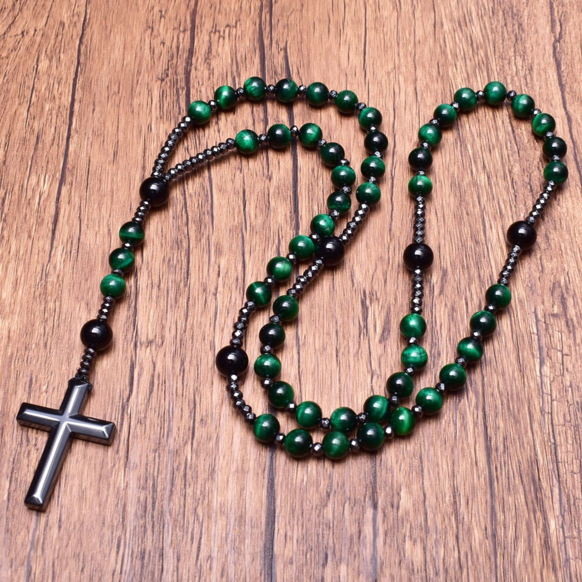 Grüne Rosenkranzkette mit schwarzem Kreuz, Holzperlen, religiöses Schmuckstück auf Holztisch.