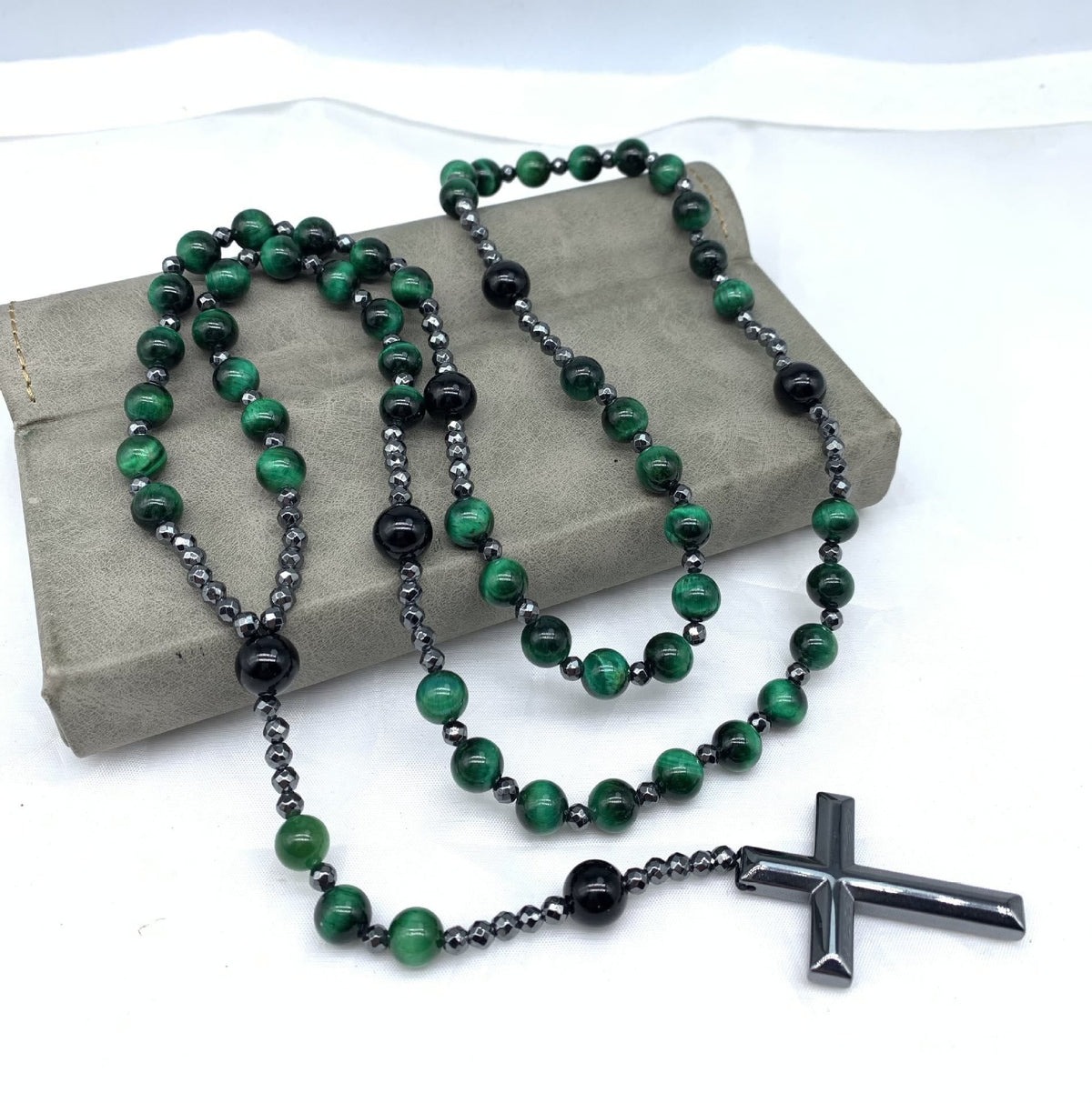 Grüne und schwarze Rosenkranzkette mit Kreuzanhänger auf grauem Hintergrund.