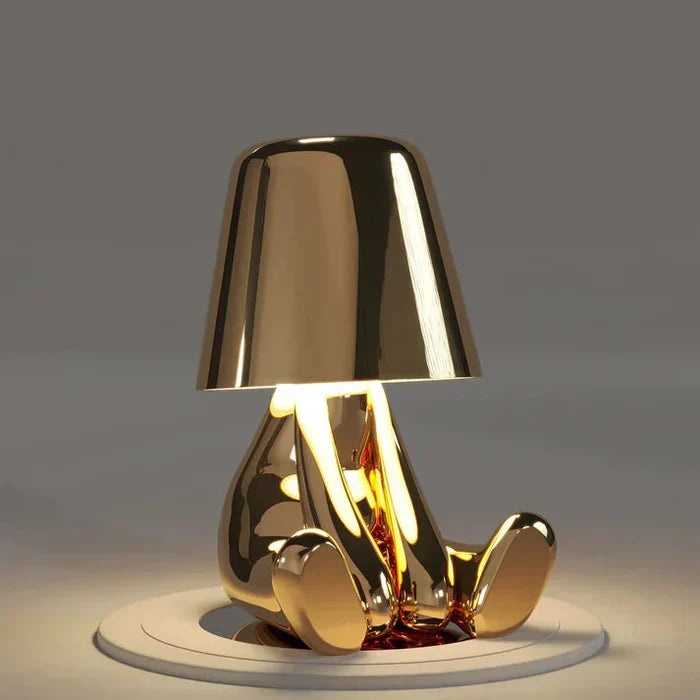 Goldene Tischlampe in Form einer sitzenden Figur, modernes Design, warmes Licht.