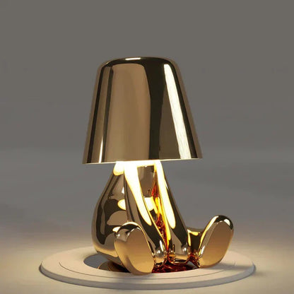 Goldene Tischlampe in Form einer sitzenden Figur, modernes Design, warmes Licht.