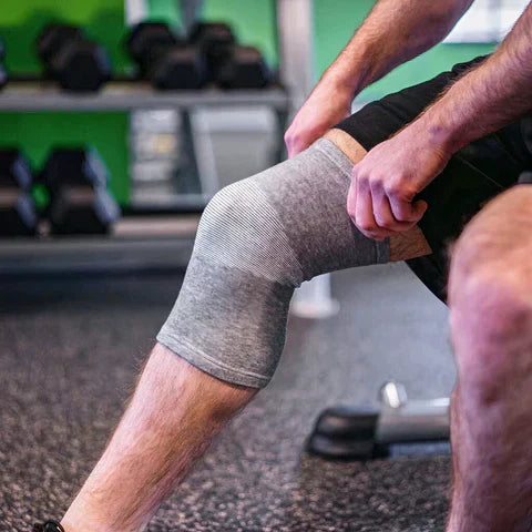 Mann im Fitnessstudio mit grauem Kniebandage, Sportbekleidung, Fitness, Rehabilitation.