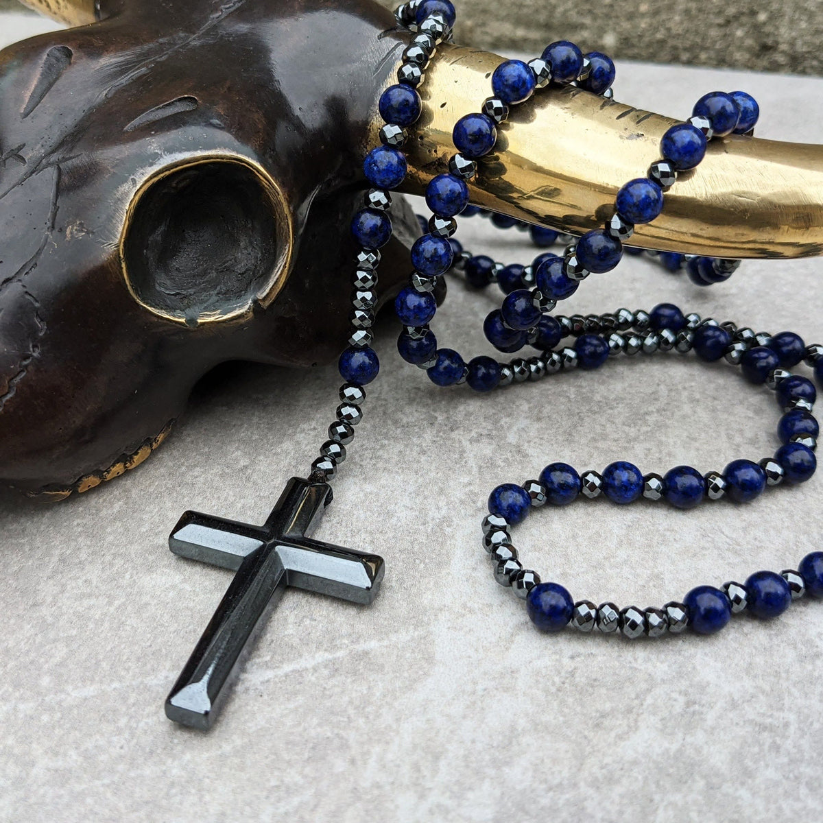 Schwarze Kreuzkette mit blauen Perlen auf Stierhorn, modisches Schmuckdesign.