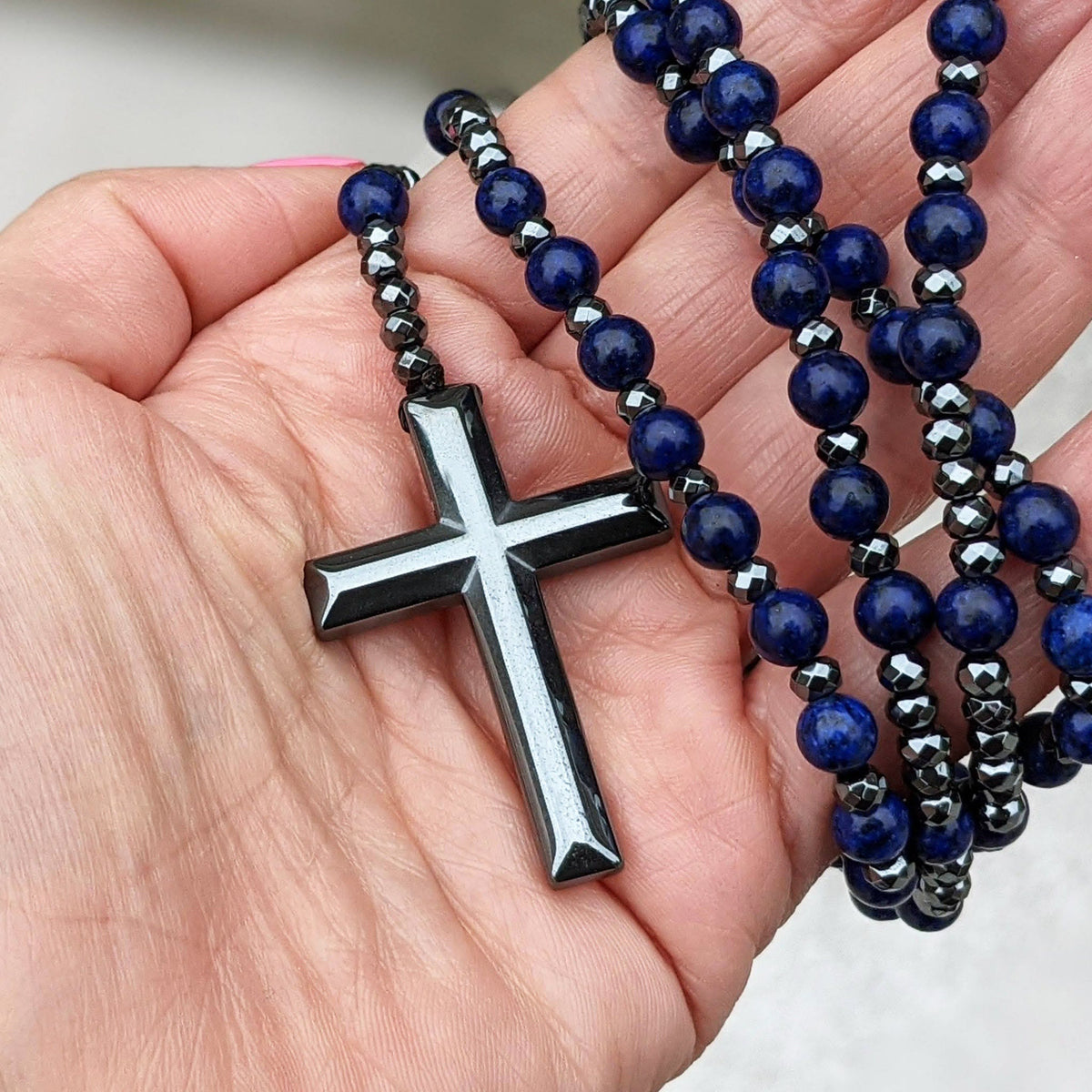 Hand hält blauen Rosenkranz mit schwarzem Kreuzanhänger, religiöses Schmuckstück, Gebetskette.